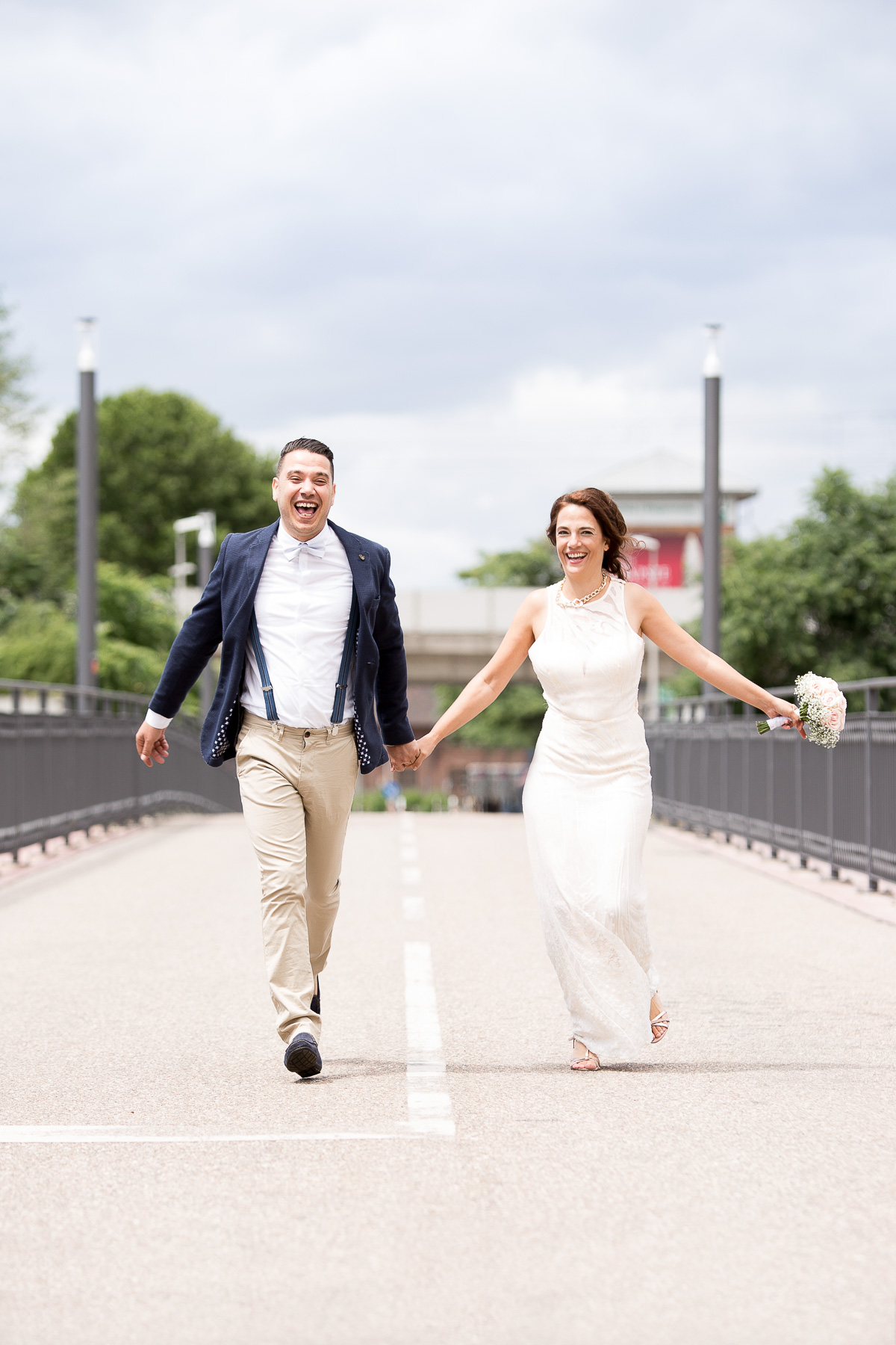 Ein Brautpaar hält Händchen und rennt lachend auf die Kamera zu.