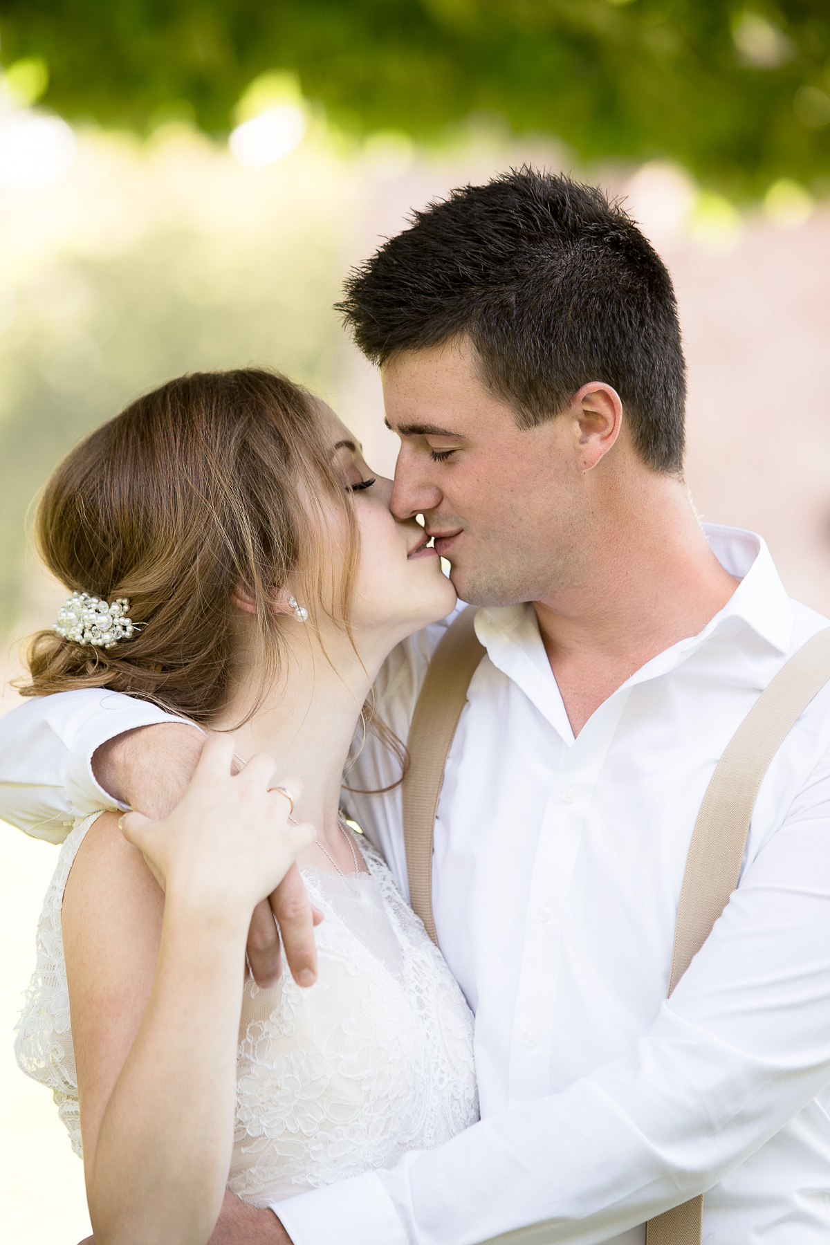 Ein Hochzeitspaar küsst sich sinnlich. Währenddessen umarmt der Bräutigam die Braut. Sie erwidert seine Umarmung, indem sie an seiner Hand fasst.