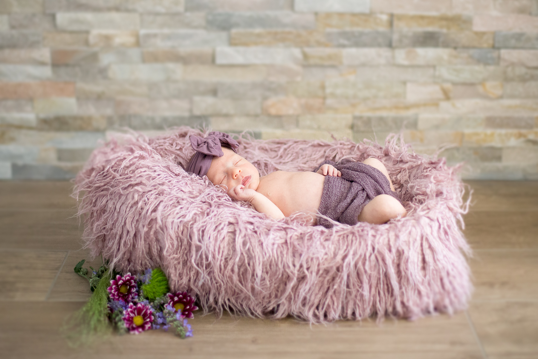 Neugeborenes Kleinkind mit Babybekleidung schlafend im dekorierten Fellbettchen mit Wiesenblumen