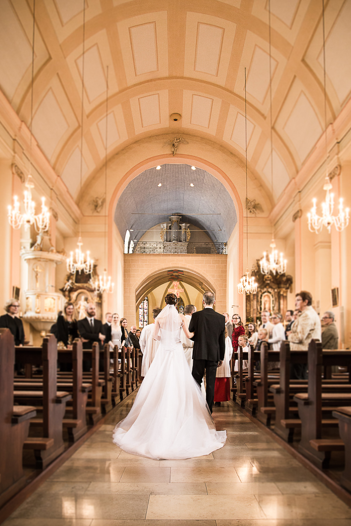 Die Braut betritt den Kirchensaal, geführt durch ihren Vater. Alle Gäste stehen und schauen auf die Braut.