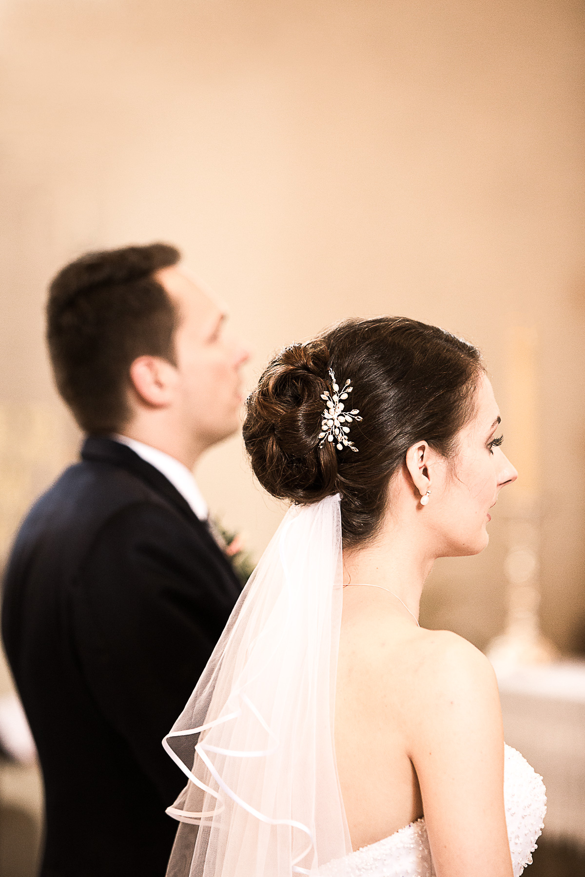 Die seitliche Rückennahansicht von der Braut. Sie hat eine elegante Hochsteckfrisur mit Haarbrosche und offenem Schleier.