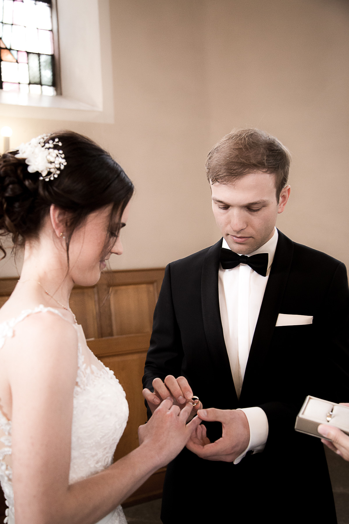 Der Bräutigam hält mit einer Hand die Hand der Braut fest und stecken mit der anderen Hand den Ehering auf den Ringfinger der Braut auf.