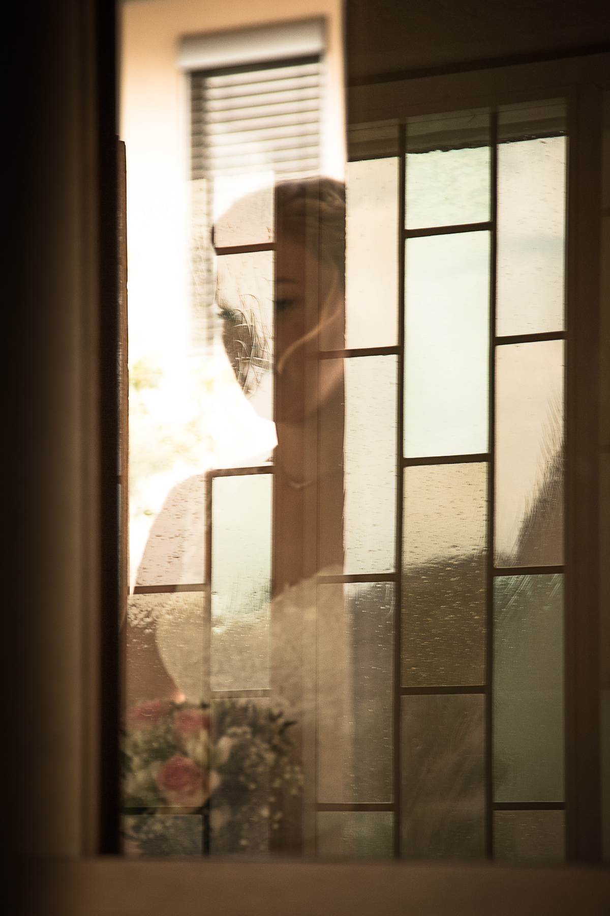 Die Braut wartet hinter der Kircheneingangstür auf ihren Eintritt in den Kirchensaal. Sie ist hinter den Gläsern der Tür teils silhouettenhaft erkennbar.