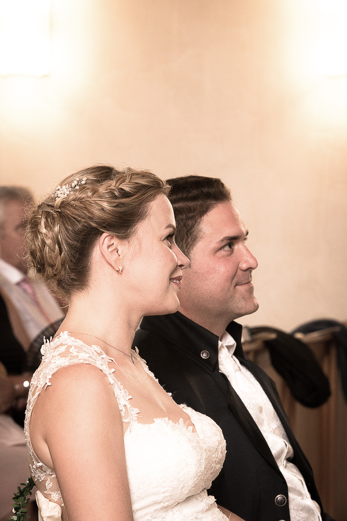 Die Braut und der Bräutigam hören während der kirchlichen Trauung dem Priester zu und haben dabei ein Lächeln im Gesicht.
