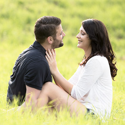 Ein junges Paar kuschelt sich im Feld an einander. Sie sitzen in einem Feld und schauen sich gegenseitig an.