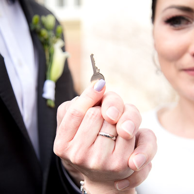 Hochzeitsreportage - Ein Brautpaar hält gemeinsam den Schlüssel ihres Liebesschlosses in ihren Händen hoch.