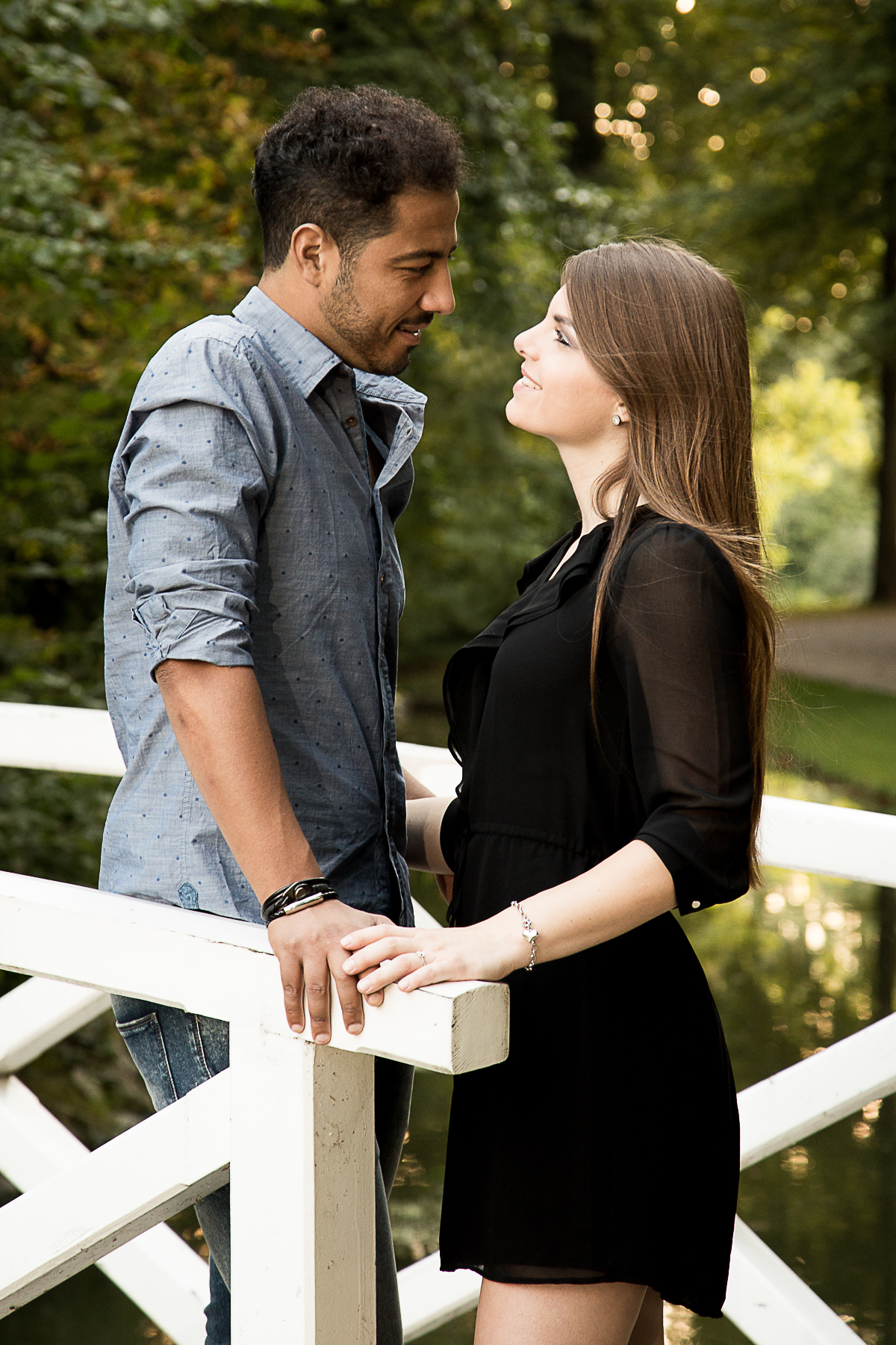 Ein junges Liebespaar steht auf einer Holzbrücke in einem Park. Sie berühren sich an den Händen und schauen gegenseitig in die Augen.