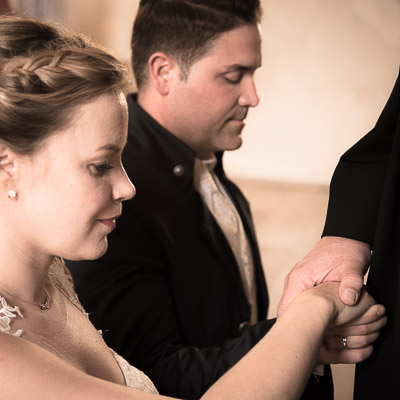 fotograf für hochzeit: Das Traupaar kniet vor dem Priester nieder und legt dabei mit geschlossenen Augen ihre Hände übereinander. Auf ihren Händen liegt die Hand des Priesters.