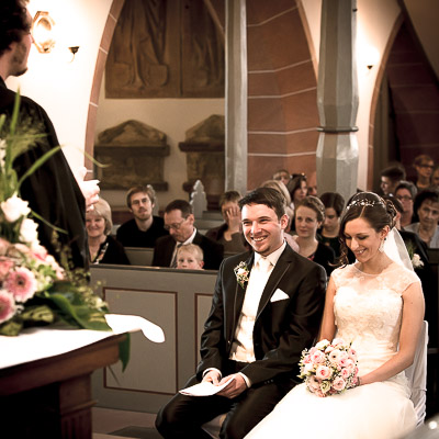 Fotografen Hochzeit: Der Priester steht vor dem Hochzeitspaar und erzählt. Die Braut und der Bräutigam lachen.